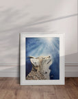 White framed artwork by Kris Horton of a bobcat looking up into sunbeams with blue background displayed leaning against the wall.