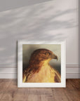 White framed painting by Kris Horton leaning against a wall of Watchful a close up of a red tail hawk.