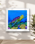 Framed artwork by Kris Horton of a turtle on a coral reef in a home setting with plants.